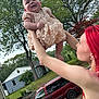 arms, baby, car, child, daylight, dress, face, grass, happy, holding, house, nature, outdoor, person, portrait, red_hair, sky, smile, trees, woman