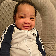 Neziah joined the competition — help win amazing prizes! baby, infant, child, smiling, portrait, close_up, curly_hair, face, eyes, nose, mouth, onesie, sportswear,  adidas_logo, blanket, couch, indoors, sitting, happy, cozy