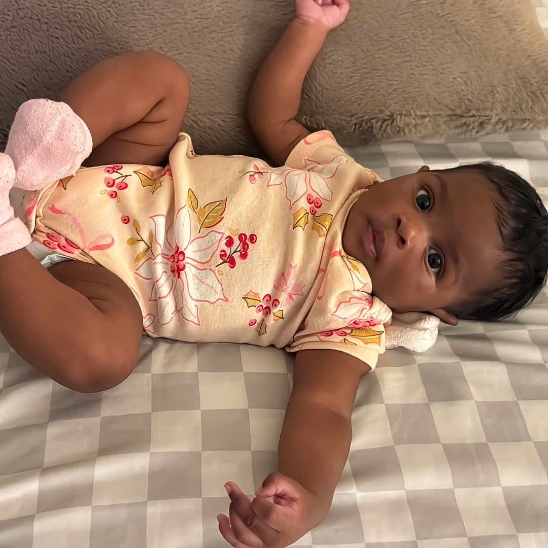 Addeline Rose joined the competition — help win amazing prizes! baby, bed, bedspread, checkered, child, curious, cute, floral_pattern, indoors, infant, lying_down, onesie, person, pillow, portrait, reaching, skin, sleeping_area, socks, young