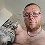 man, beard, glasses, shirtless, cat, tabby_cat, indoor, portrait, closeup, pet, feline, green_eyes, chain_necklace, hairy_chest, calm, looking_away, human, animal, companion, casual