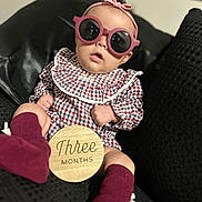Renesmee joined the competition — help win amazing prizes! baby, infant, sunglasses, headband, plaid_clothing, sitting, couch, black_furniture, wooden_sign, three_months, maroon_socks, indoor, portrait, child, cute, fashion, accessory, young_child, home, soft_lighting