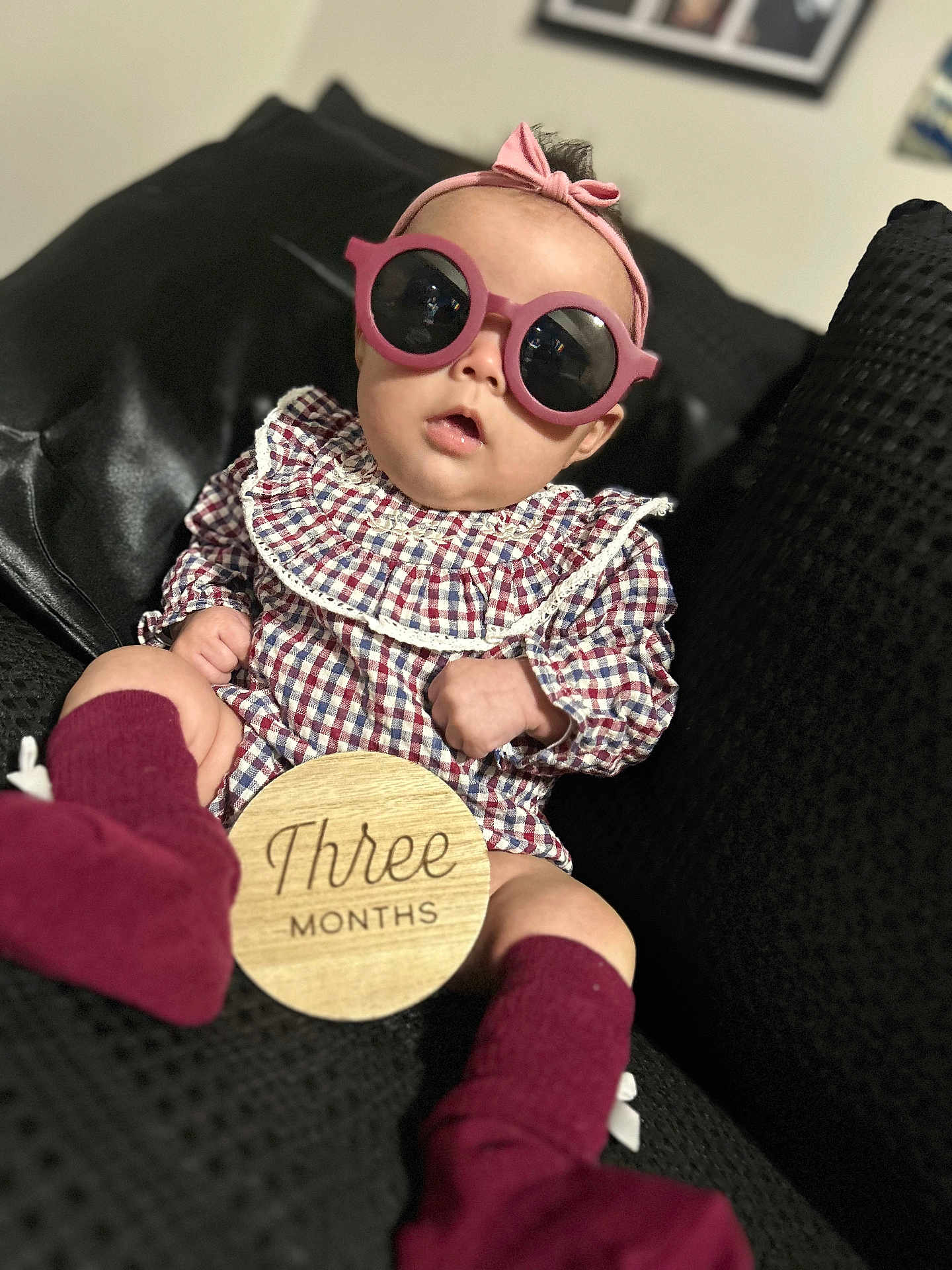 Renesmee joined the competition — help win amazing prizes! baby, infant, sunglasses, headband, plaid_clothing, sitting, couch, black_furniture, wooden_sign, three_months, maroon_socks, indoor, portrait, child, cute, fashion, accessory, young_child, home, soft_lighting