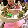 baby, child, smile, leopard_print, walker, toy, indoor, happy, face, person, playful, infant, clothing, furniture, floor, activity_center, bright, cute, seat, expression