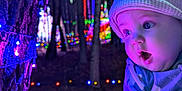 Kayden is registered to the contest to win money with this photo: baby, child, winter_clothing, hat, tree, holiday_lights, colorful_lights, bokeh, forest, night, outdoor, curious, face, portrait, glowing, cozy, cute, expression, nature, warm_clothes