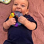 baby, infant, teething_toy, smiling, diaper, pampers, blue_shirt, blanket, play, cute, hand, face, child, lying_down, happy, indoors, toy, colorful, young_child, bib