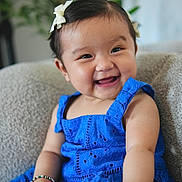 Zeya is registered to the contest to win money with this photo: baby, background_plant, blue_dress, bracelet, child, cozy, cute, expression, face, furniture, hair_bow, happy, indoor, person, portrait, sitting, skin, smiling, toddler, young_child