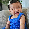 baby, background_plant, blue_dress, bracelet, child, cozy, cute, expression, face, furniture, hair_bow, happy, indoor, person, portrait, sitting, skin, smiling, toddler, young_child