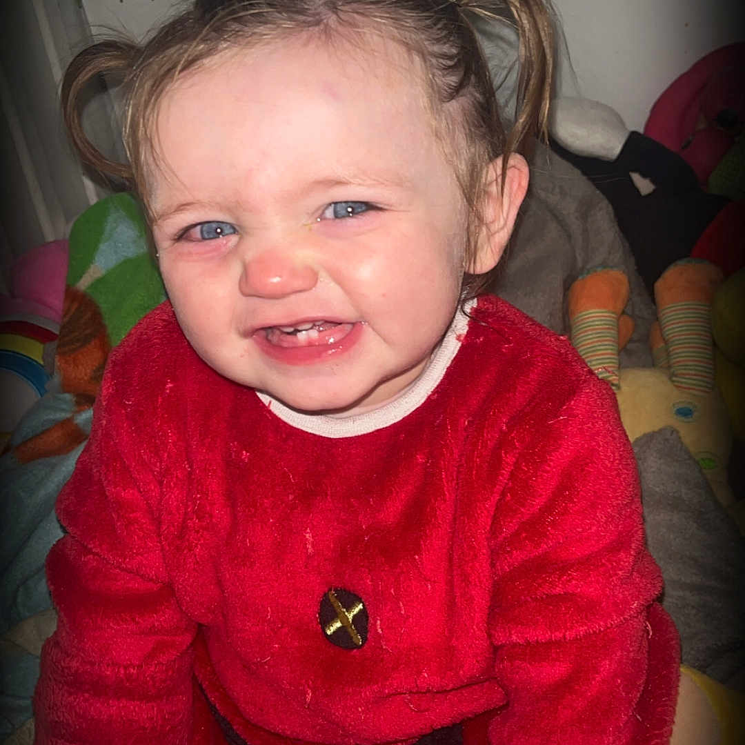 Kayana participe au concours pour gagner de l'argent avec cette photo : baby, blanket, blue_eyes, child, cozy, cute, expression, face, happy, indoors, person, pigtails, playful, portrait, red_clothing, sitting, smiling, soft_toys, toddler, young_child