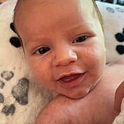 Trustyn is registered to the contest to win money with this photo: baby, infant, smiling, close_up, face, skin, blanket, soft, cute, happy, eyes, mouth, arm, newborn, indoors, blurred_background, heart_pattern, person, child, portrait