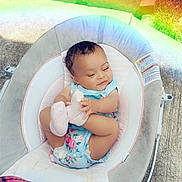 Jamaya joined the competition — help win amazing prizes! baby, child, infant, baby_seat, floral_clothing, outdoor, sidewalk, grass, rainbow_light, pink_socks, smiling, happy, cute, playful, person, foot, seat, fabric, blanket, sunlight