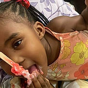 Amora is registered to the contest to win money with this photo: child, girl, smiling, eating, lollipop, candy, dessert, food, bed, bedroom, floral, blanket, braids, hair_accessories, pink, orange, portrait, indoors, sitting, happy