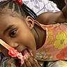 child, girl, smiling, eating, lollipop, candy, dessert, food, bed, bedroom, floral, blanket, braids, hair_accessories, pink, orange, portrait, indoors, sitting, happy