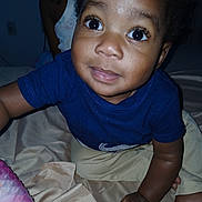 Orion joined the competition — help win amazing prizes! baby, child, infant, portrait, face, eyes, wide_eyes, curious, smiling, blue_shirt, short_sleeves, sitting, bed, bedding, bedroom, indoor, flash_photography, dark_background, baby_hands, close_up