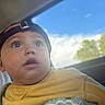 Danilo is registered to the contest to win money with this photo: baby, infant, child, portrait, face, wide_eyed, looking_up, black_cap, yellow_clothing, car, car_seat, window, blue_sky, clouds, greenery, outdoor, close_up, head, sitting, safe