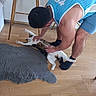 animal, bare_arms, casual_clothing, cat, comfort, domestic, floor, furniture, home, human_pet_interaction, indoor, interaction, man, pet, playful, relaxation, rug, socks, stretching, wooden_floor