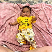 Khylan is registered to the contest to win money with this photo: baby, child, smiling, yellow_clothing, bee_pattern, pink_blanket, lying_down, happy, cute, infant, soft_texture, indoors, playful, person, toddler, cozy, blanket, socks, legs, raised_hand