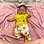 baby, child, smiling, yellow_clothing, bee_pattern, pink_blanket, lying_down, happy, cute, infant, soft_texture, indoors, playful, person, toddler, cozy, blanket, socks, legs, raised_hand
