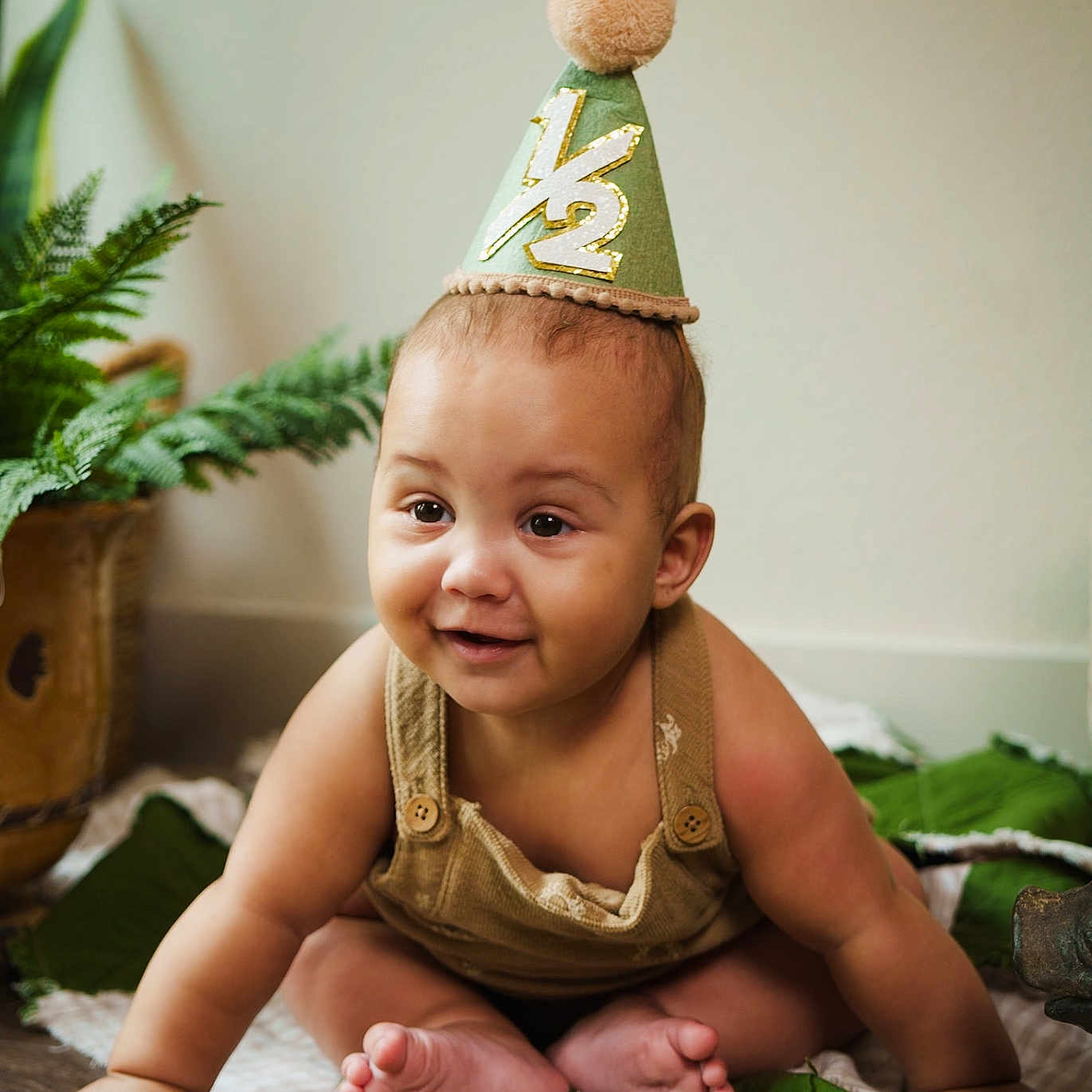 Case joined the competition — help win amazing prizes! baby, child, party_hat, half_birthday, smiling, sitting, indoors, plant, blanket, floor, cute, portrait, happy, young_child, casual_clothing, crawling, green, decor, infant, celebration