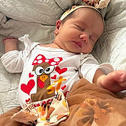 Stella is registered to the contest to win money with this photo: baby, sleeping, headband, white_blanket, cartoon, hearts, cute_outfit, skirt, infant, peaceful, closeup, soft_texture, child, apparel, resting, adorable, face, person, indoors, newborn