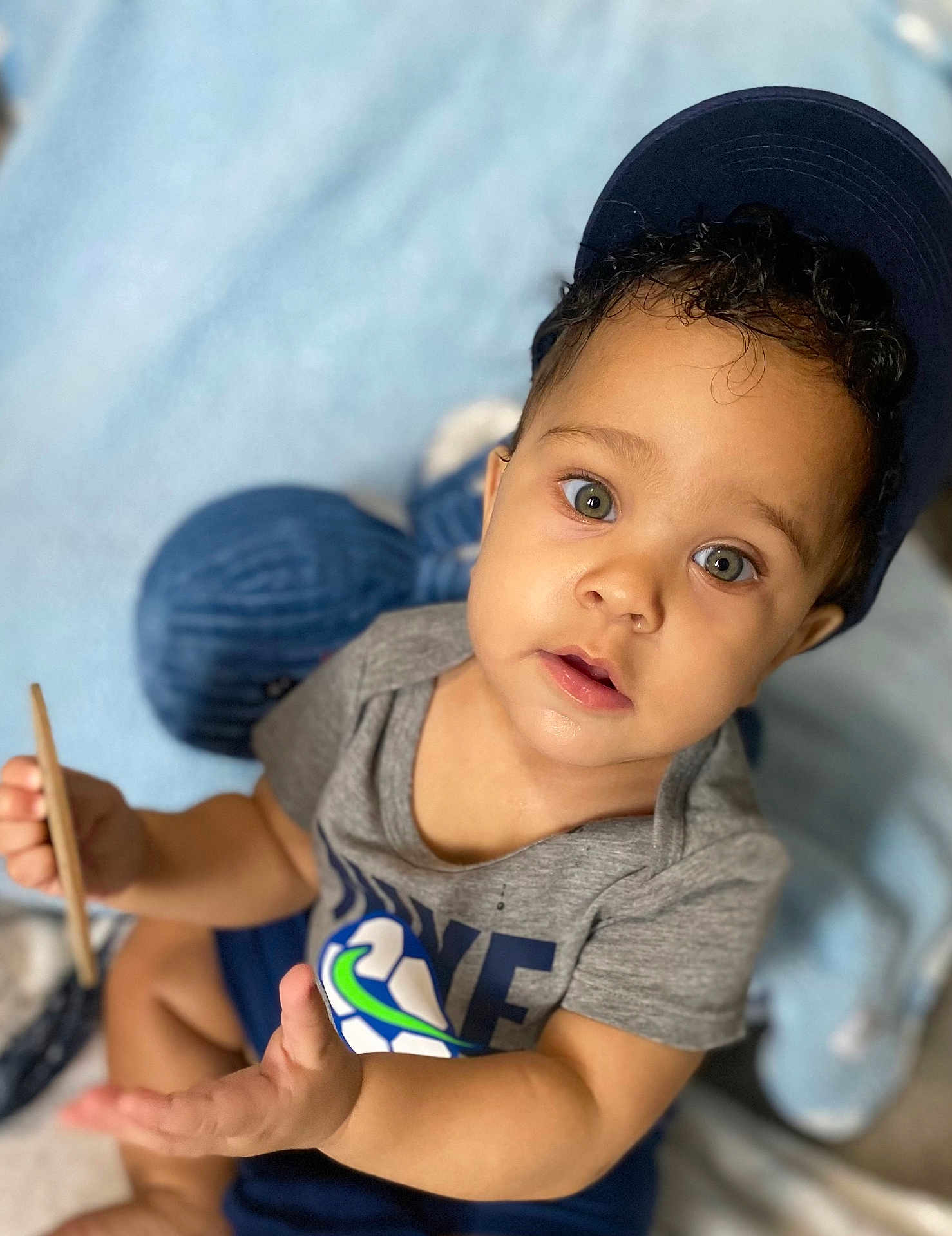 Hunter joined the competition — help win amazing prizes! toddler, child, cap, curious, indoor, soft_blanket, toy, holding_object, green_eyes, grey_shirt, navy_shorts, cute, portrait, baby, sitting, hand, face, expression, curly_hair, closeup