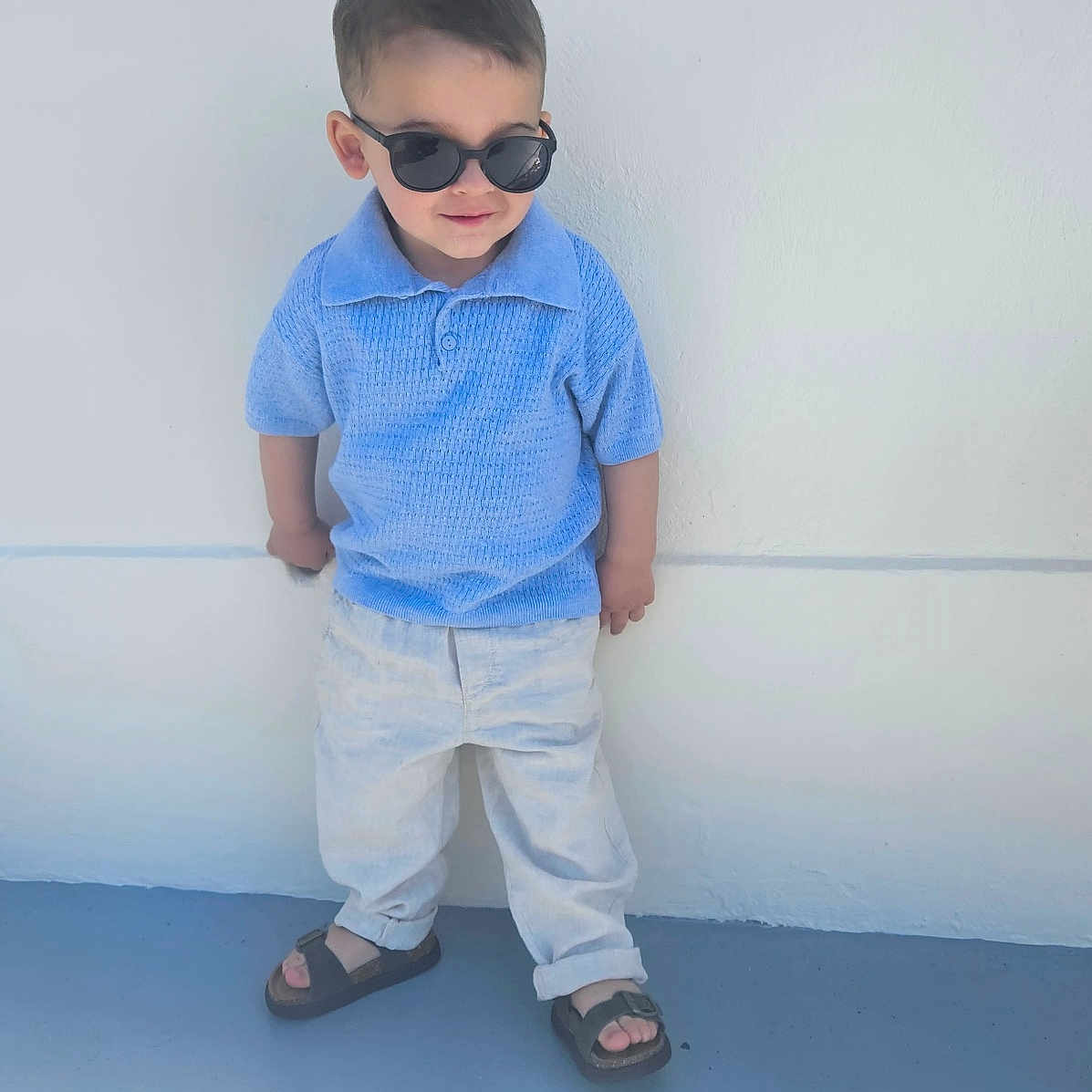 Ethan participe au concours pour gagner de l'argent avec cette photo : blue_shirt, casual_clothing, child, confident, cool, cute, fashion, outdoor, pants, person, portrait, sandals, shadow, short_hair, standing, summer, sunglasses, sunlight, toddler, white_wall
