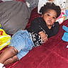 Isayana is registered to the contest to win money with this photo: child, baby, sibling, couch, pillow, blanket, indoor, relaxed, smiling, denim_shorts, black_shirt, white_shirt, curly_hair, braided_hair, red_couch, home, portrait, laying_down, casual, family