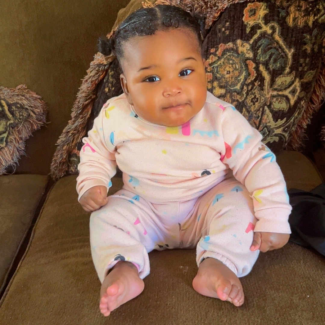 Isayana joined the competition — help win amazing prizes! baby, child, sitting, couch, indoors, cozy, onesie, pastel_colors, patterned_clothing, curly_hair, smiling, cute, young_child, furniture, home, portrait, comfortable, happy, face, feet
