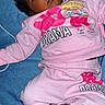 baby, child, infant, pink_clothing, sweatshirt, sweatpants, blue_towel, pacifier, wide_eyes, expression, lying_down, cute, casual_wear, indoor, person, face, foot, hand, curly_hair, drama