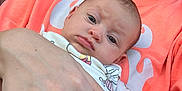 Cleo is registered to the contest to win money with this photo: baby, infant, person, hand, clothing, orange_shirt, face, eyes, skin, portrait, holding, cuddle, child, newborn, expression, casual, indoor, closeup, human, apparel