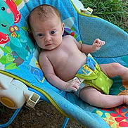 Cleo is registered to the contest to win money with this photo: baby, infant, child, baby_rocker, outdoor, grass, dirt, colorful, patterned_fabric, flowers, animals, blue, green, yellow, bare_chest, curious, sitting, person, young_child, playful