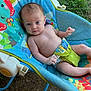 baby, infant, child, baby_rocker, outdoor, grass, dirt, colorful, patterned_fabric, flowers, animals, blue, green, yellow, bare_chest, curious, sitting, person, young_child, playful