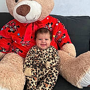 Genesis is registered to the contest to win money with this photo: baby, leopard_print, onesie, smile, teddy_bear, plush_toy, red_sweater, mickey_mouse, couch, indoor, happy, child, cute, toy, soft, furniture, seated, person, cozy, portrait