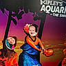 baby, woman, face_cutout, photo_board, tropical, sunset, aquarium, portrait, smiling, angry_face, costume, flower, vibrant_colors, humor, playful, people, posing, signage, exaggerated_expression, indoor