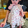 Vivian is registered to the contest to win money with this photo: baby, child, person, adult, smile, dress, headband, butterfly_pattern, floor, wooden_floor, indoor, holding_hand, support, sitting, tattoo, fan, cage, happy, family, bonding