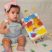 Chloe is registered to the contest to win money with this photo: baby, child, pink_bow, paint, colorful, milestone, first_month, overalls, sitting, barefoot, face, curious, art, canvas, easel, color_splatter, indoors, cute, celebration, portrait