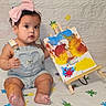 baby, child, pink_bow, paint, colorful, milestone, first_month, overalls, sitting, barefoot, face, curious, art, canvas, easel, color_splatter, indoors, cute, celebration, portrait