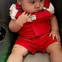 baby, child, car_seat, red_overalls, white_shoes, converse, bow, hair_accessory, cute, infant, sitting, clothing, footwear, chubby_cheeks, portrait, indoors, curious, cute_expression, person, baby_fashion