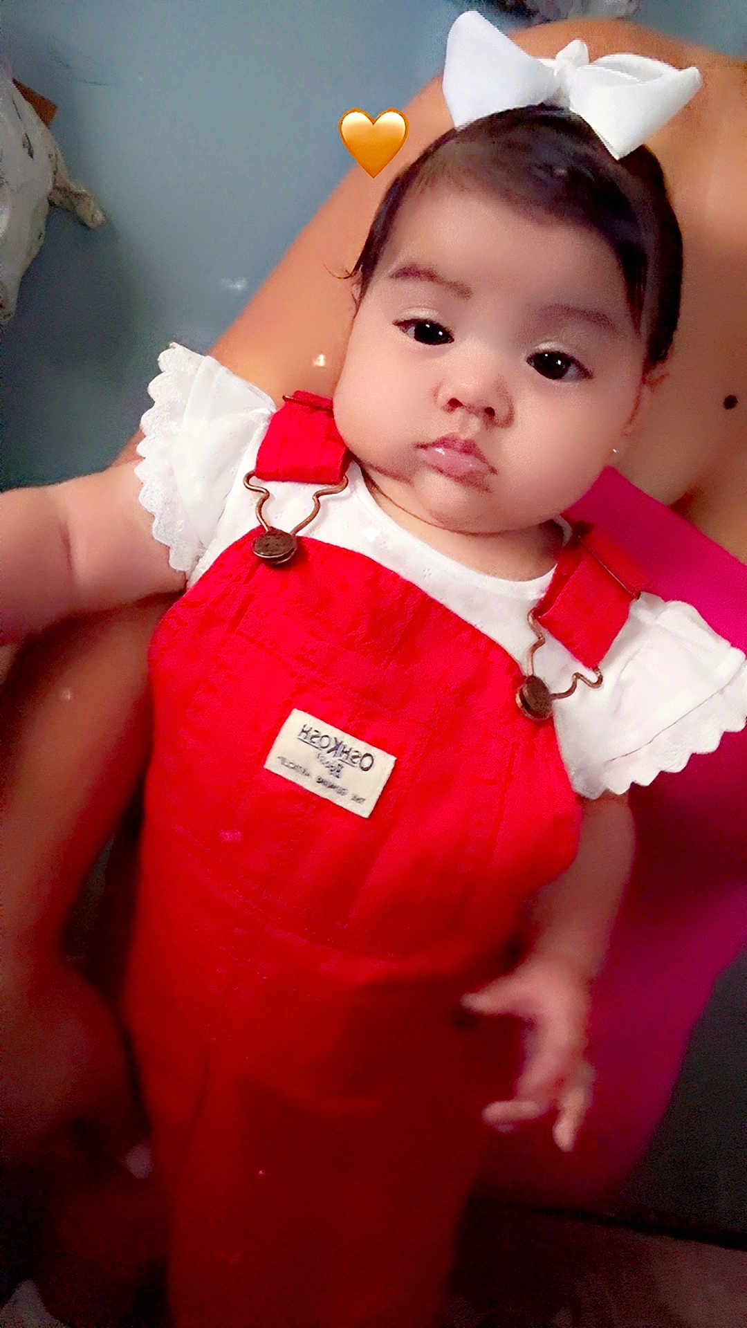 Jaylen is registered to the contest to win money with this photo: baby, child, red_overalls, white_bow, infant, cute, person, hand, pink_clothing, skin, face, eyes, indoors, closeup, portrait, holding, love_emoji, young_child, adorable, casual_clothing