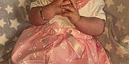 Aria-Louise is registered to the contest to win money with this photo: baby, infant, child, pink_dress, white_socks, bracelet, blanket, star_pattern, hands, face, portrait, cute, lying_down, soft_texture, fabric, clothing, person, indoor, newborn, expression