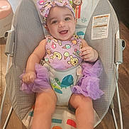 Trinity is registered to the contest to win money with this photo: baby, infant, smiling, child, bouncer, purple_clothing, headband, tutu, indoor, wooden_floor, cute, happy, person, face, seat, playful, animal_print, toddler, sitting, joyful