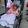 baby, stroller, blanket, toy, unicorn, pink_jacket, hair_ties, outdoor, pavement, child, infant, cute, person, seat, accessory, footwear, clothing, playful, bundle, curious