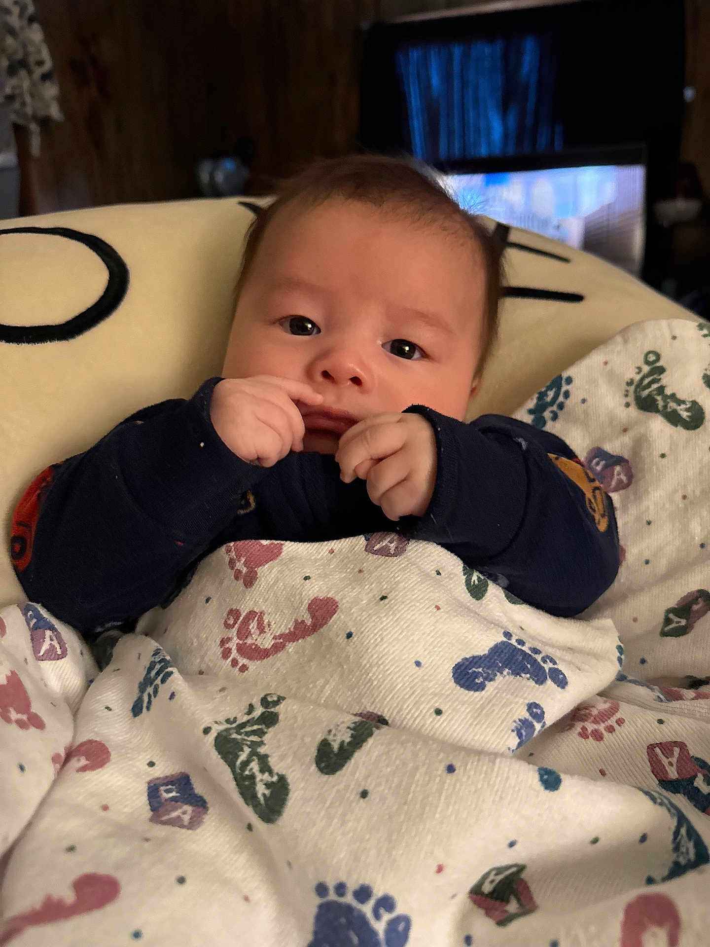 Treyvon joined the competition — help win amazing prizes! baby, infant, blanket, footprint_pattern, hands, face, indoor, cozy, curious, portrait, child, clothing, soft_lighting, couch, home, young, sitting, comfort, wrapped, cute