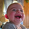 baby, child, laughing, indoor, face, closeup, curtains, wood_paneling, smile, cheeks, person, infant, happy, expression, clothing, head, mouth, tongue, skin, hand