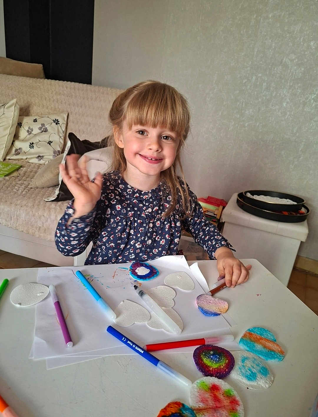 Clary participe au concours pour gagner de l'argent avec cette photo : child, girl, smiling, waving, craft, markers, paint, table, heart_shapes, paper, living_room, cushions, sofa, art, colorful, happy, indoor, person, hair, clothing