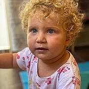 Emelin participe au concours pour gagner de l'argent avec cette photo : child, curly_hair, blonde_hair, blue_eyes, portrait, indoor, toddler, cute, face, person, clothing, white_shirt, floral_pattern, expression, looking_away, soft_background, skin, head, young, innocent