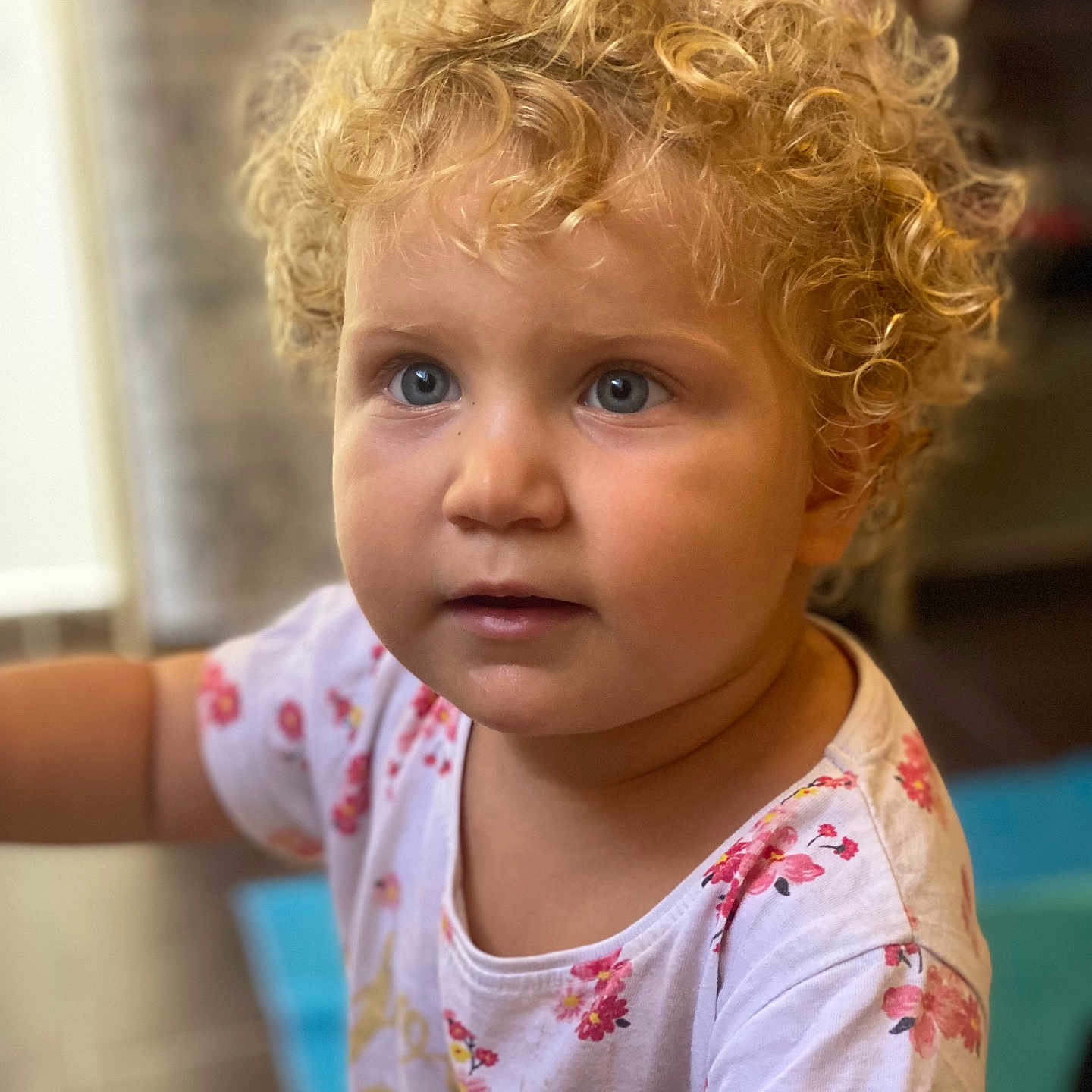 Emelin participe au concours pour gagner de l'argent avec cette photo : blonde_hair, blue_eyes, child, clothing, curly_hair, cute, expression, face, floral_pattern, head, indoor, innocent, looking_away, person, portrait, skin, soft_background, toddler, white_shirt, young