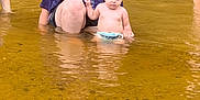 Elana is registered to the contest to win money with this photo: adult, baby, bathing, clothing, face, female, head, nature, outdoors, person, photography, portrait, ripple, sea, shorts, soil, summer, swimwear, water, woman