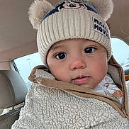 John is registered to the contest to win money with this photo: baby, child, hat, mickey_mouse, pom_poms, jacket, sherpa, cozy, face, eyes, car_interior, seat, clothing, winter_wear, cute, portrait, young_child, warm, close_up, infant