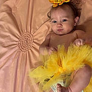 Oakley is registered to the contest to win money with this photo: baby, tutu, yellow, flower_headband, diaper, blanket, soft_texture, infant, cute, smile, lying_down, child, skin, foot, hand, face, head, indoors, comfortable, portrait