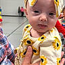 baby, background, balloons, blurred, child, clothing, curious_expression, cute, hand, headband, holding, indoor, infant, outfit, people, person, plaid_shirt, portrait, sunflower, tongue_out
